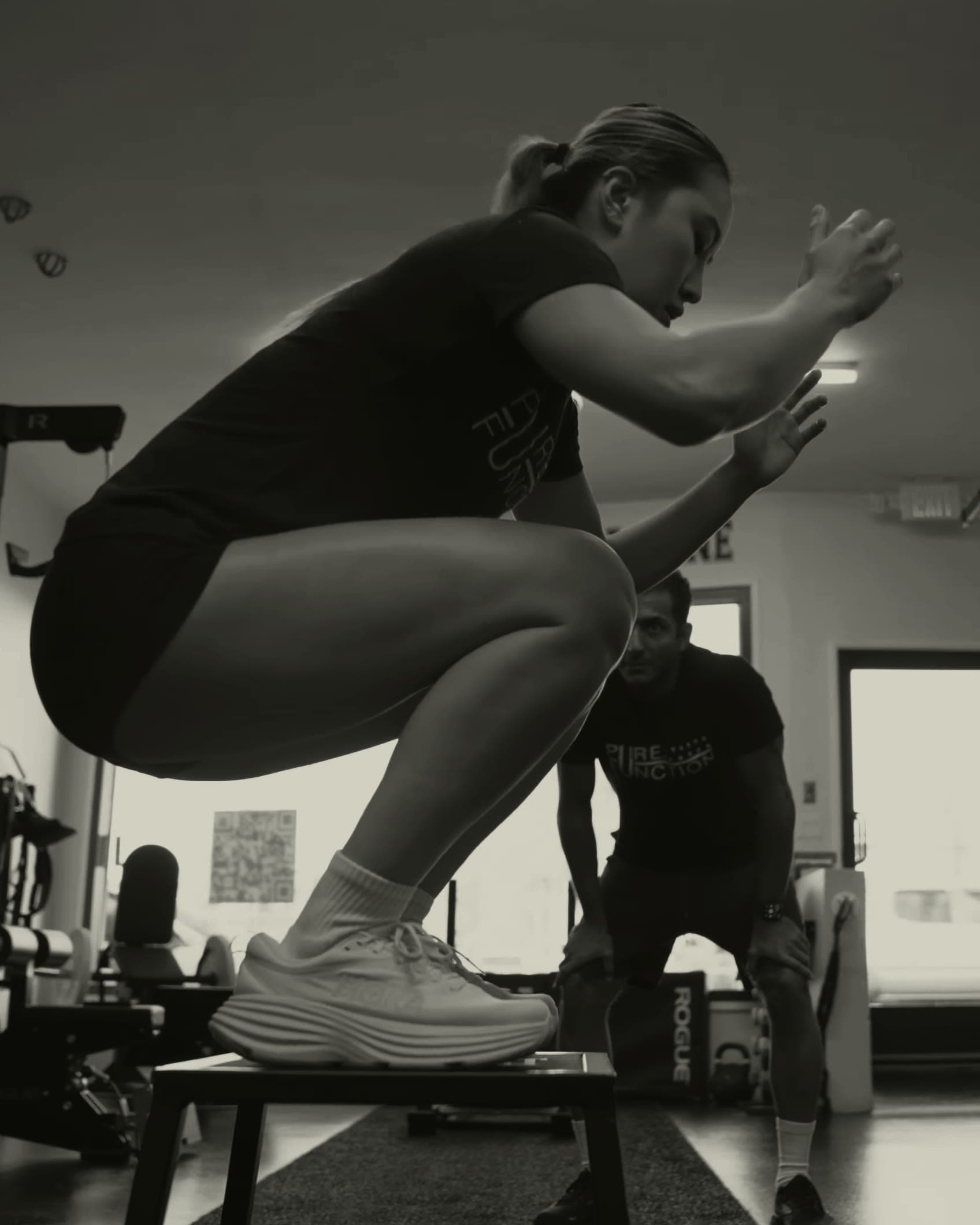 Athlete landing a box jump in a deep catch while a Pure Function coach evaluates the movement