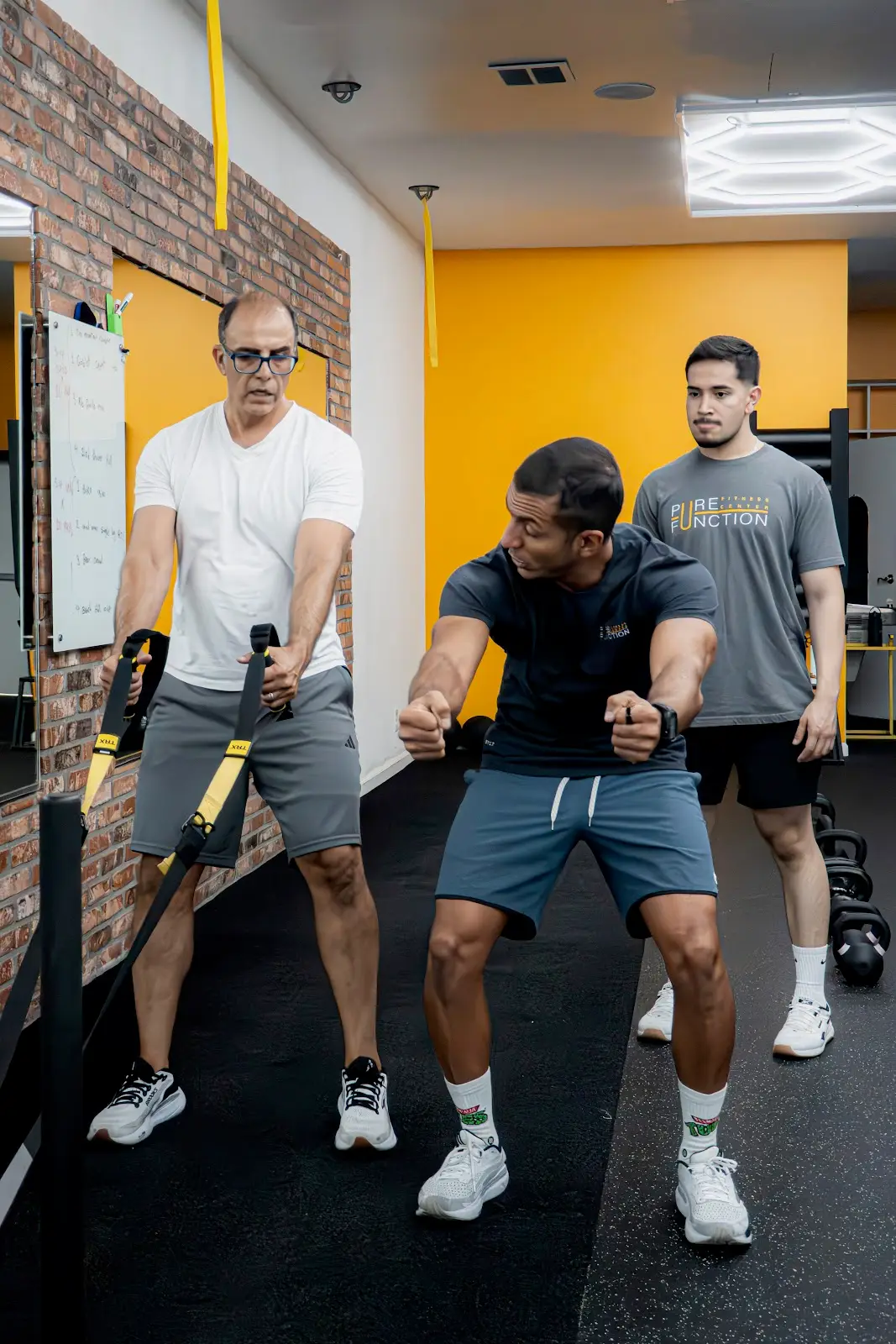 A Pure Function coach cueing two clients through TRX work