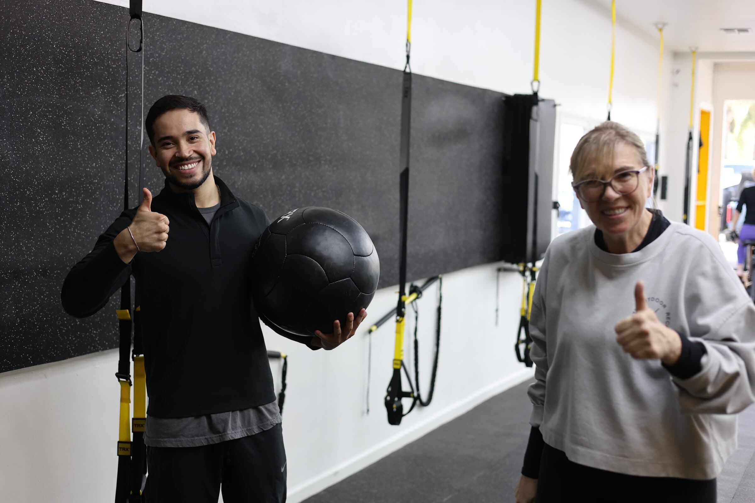 A Pure Function coach and client smiling with thumbs up after a session